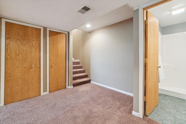 finished below grade area featuring a textured ceiling, visible vents, carpet, baseboards, and stairs