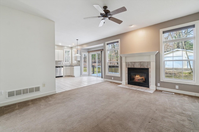 unfurnished living room with baseboards, visible vents, a tiled fireplace, a ceiling fan, and light carpet