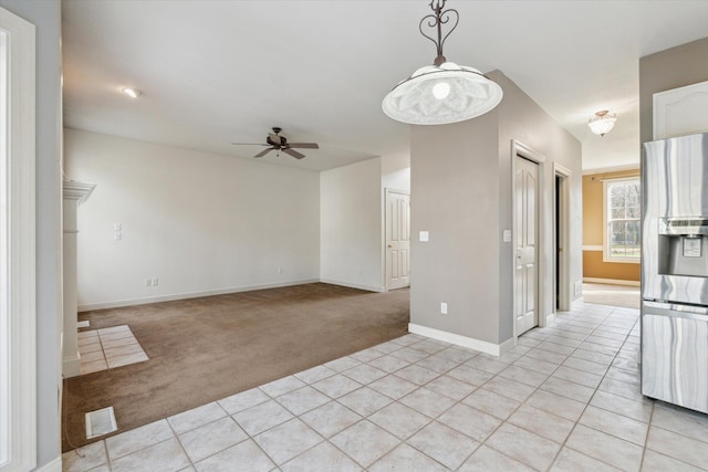 spare room featuring a ceiling fan, light tile patterned floors, light colored carpet, and visible vents