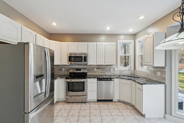 kitchen featuring decorative backsplash, white cabinets, stainless steel appliances, a sink, and light tile patterned floors
