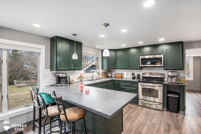 kitchen with tasteful backsplash, wood finished floors, a peninsula, stainless steel appliances, and decorative light fixtures