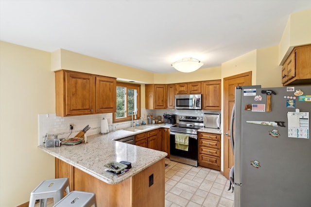 kitchen featuring a sink, stainless steel appliances, a peninsula, decorative backsplash, and a kitchen bar