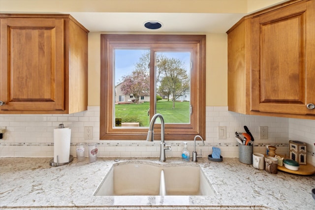 kitchen featuring a sink, brown cabinetry, and light stone countertops