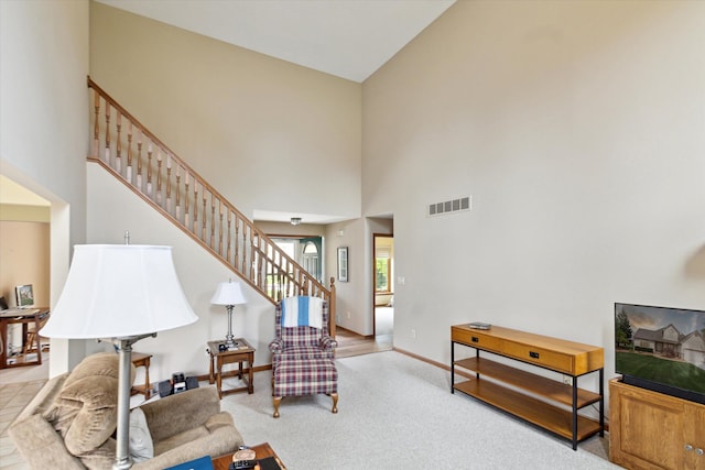 carpeted living room with baseboards, a high ceiling, stairs, and visible vents