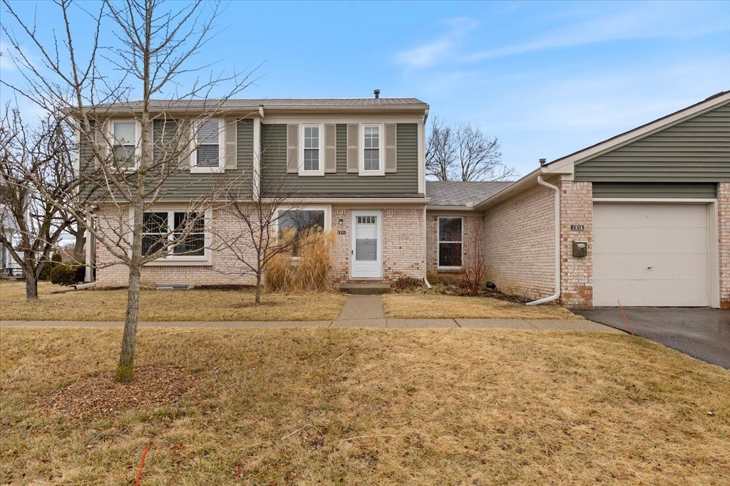 view of front facade with aphalt driveway, an attached garage, brick siding, and a front yard