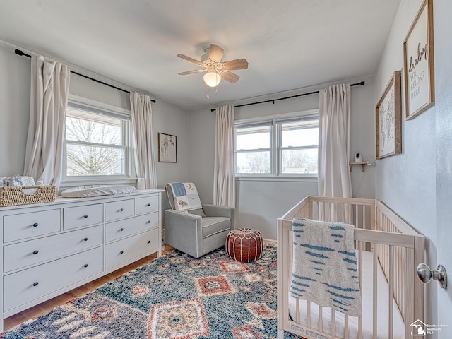 bedroom featuring wood finished floors, ceiling fan, and a nursery area