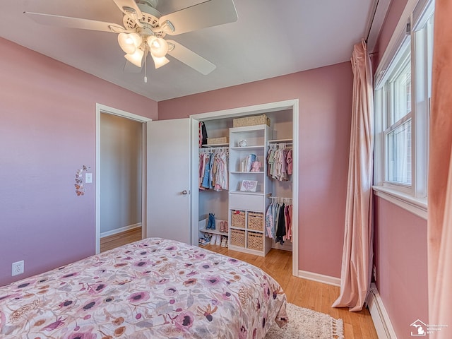 bedroom featuring a closet, light wood-style flooring, a baseboard heating unit, baseboards, and ceiling fan