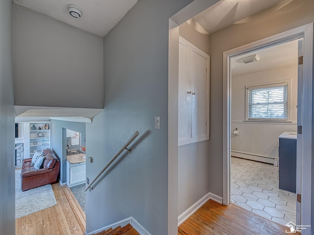 stairs with baseboards, wood finished floors, and a baseboard heating unit