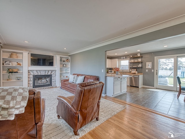 living room featuring baseboards, ornamental molding, wood finished floors, recessed lighting, and a stone fireplace