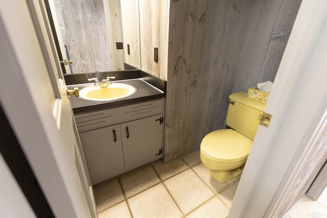 half bath with tile patterned flooring, vanity, toilet, and wood walls