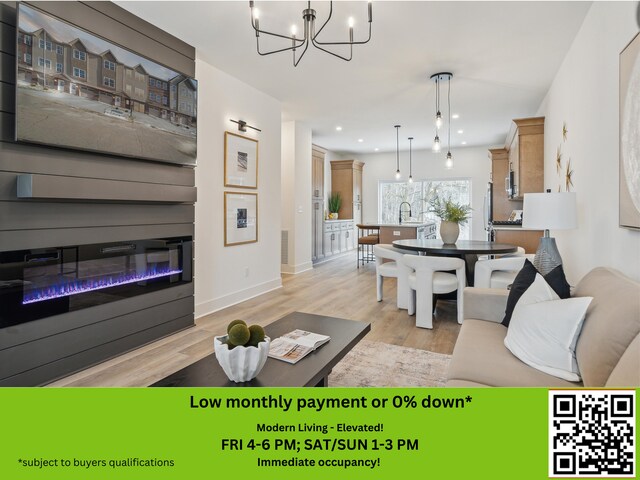 living area with a notable chandelier, a glass covered fireplace, light wood-style flooring, baseboards, and recessed lighting