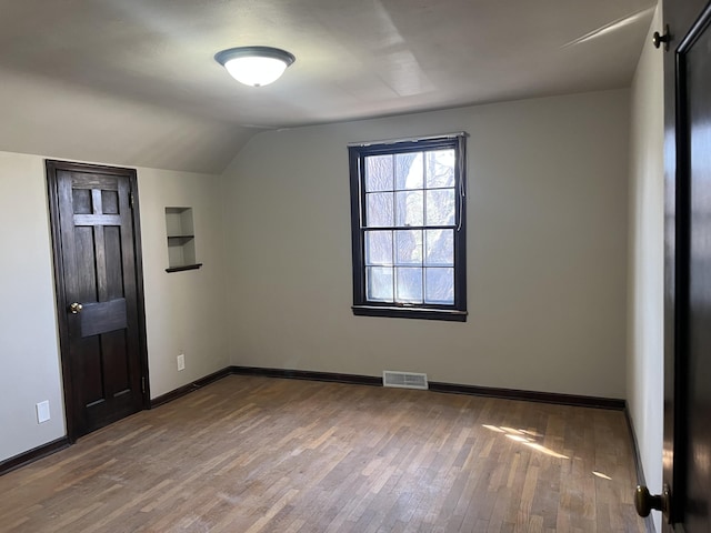 345 S Cochran Ave, Charlotte, MI 48813 - unfurnished bedroom featuring baseboards, vaulted ceiling, wood finished floors, and visible vents