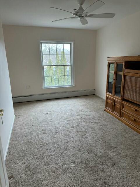 interior space featuring baseboards, ceiling fan, carpet, and a baseboard radiator