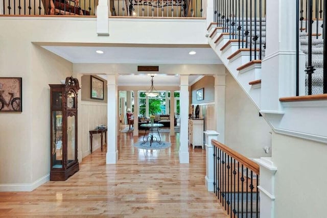 entryway with crown molding, wood finished floors, stairway, decorative columns, and a high ceiling