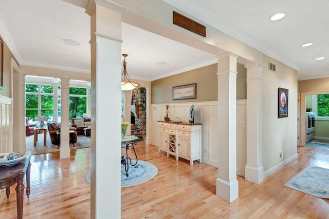interior space featuring decorative columns, ornamental molding, washer / dryer, light wood finished floors, and visible vents