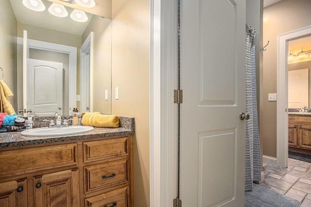 full bath featuring stone tile flooring, baseboards, and vanity