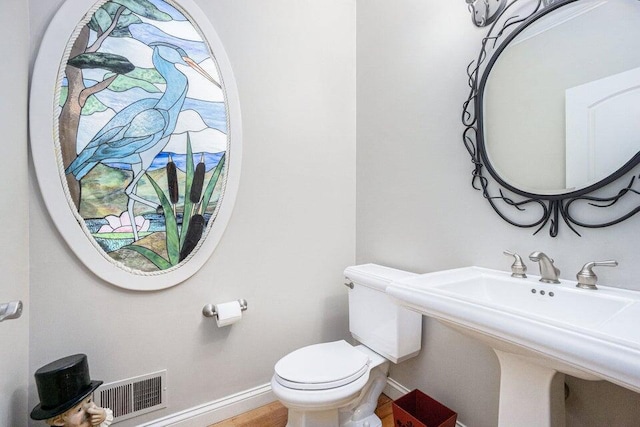 half bathroom featuring toilet, a sink, baseboards, and visible vents