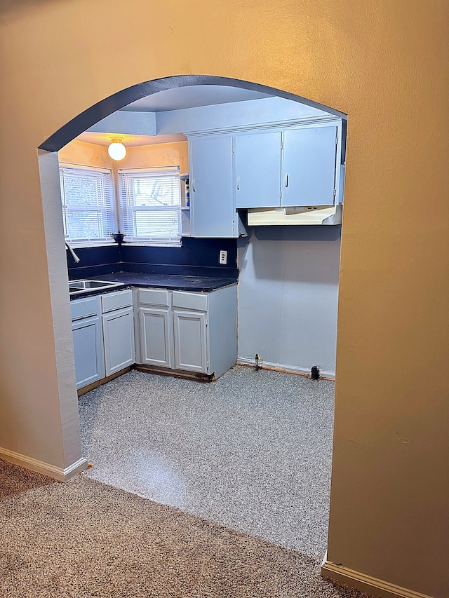 kitchen with baseboards, a sink, dark countertops, carpet floors, and arched walkways