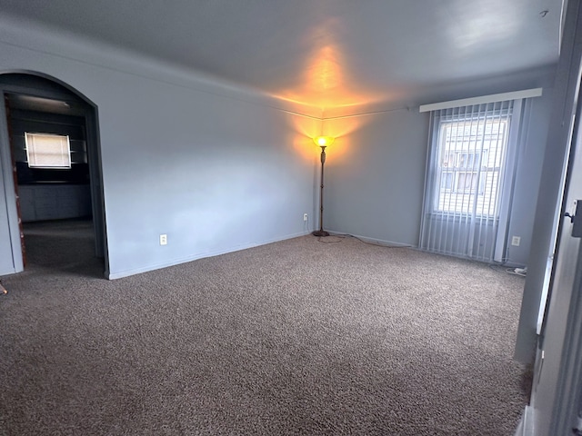 unfurnished room featuring baseboards, arched walkways, and carpet