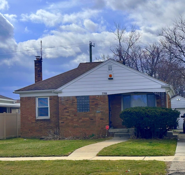 view of front of house featuring brick siding, a chimney, a front lawn, and fence