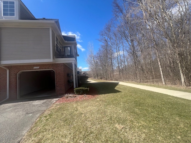 view of side of property featuring a yard, a garage, brick siding, and aphalt driveway