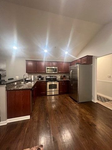 kitchen featuring dark wood-style flooring, stainless steel appliances, dark stone counters, lofted ceiling, and a sink