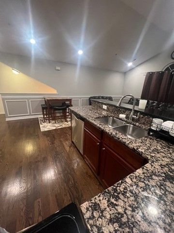 kitchen with dark wood finished floors, stainless steel dishwasher, a sink, and a wainscoted wall