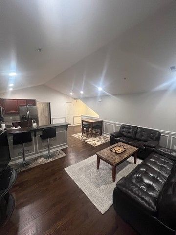 living area with a decorative wall, vaulted ceiling, and dark wood finished floors