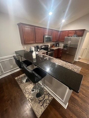 kitchen with lofted ceiling, a peninsula, dark wood-type flooring, and stainless steel appliances