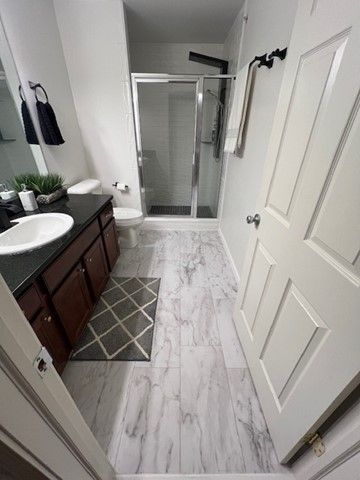 full bath with a stall shower, toilet, and vanity