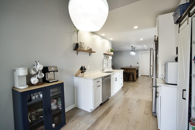kitchen with light countertops, open shelves, stainless steel dishwasher, a sink, and light wood-style floors
