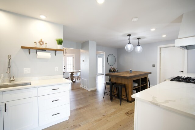 kitchen featuring a sink, open shelves, light wood finished floors, white cabinetry, and visible vents