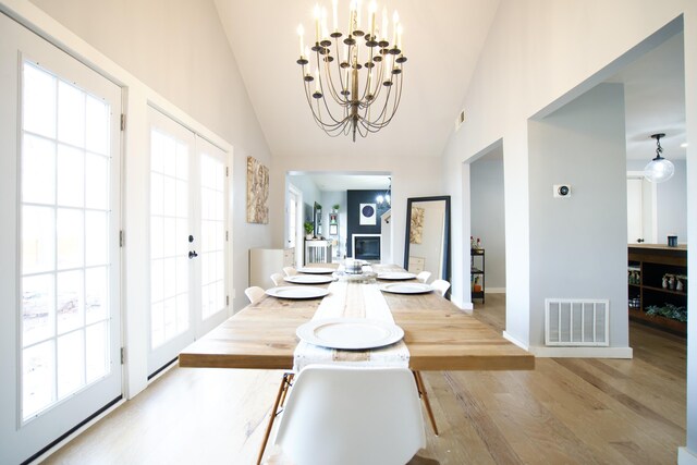 dining space featuring vaulted ceiling, a chandelier, wood finished floors, baseboards, and visible vents