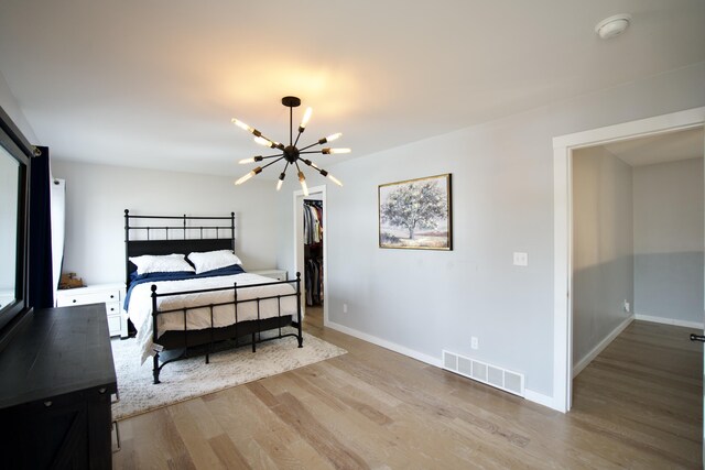 bedroom featuring a spacious closet, baseboards, a chandelier, visible vents, and wood finished floors
