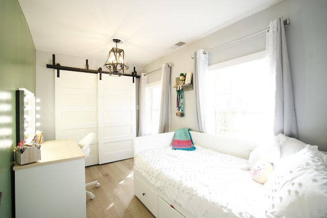 bedroom with a barn door, visible vents, and light wood-style floors