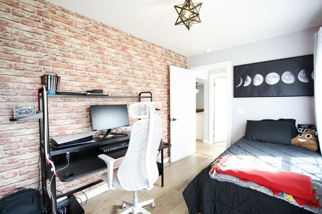 bedroom with wood finished floors and brick wall