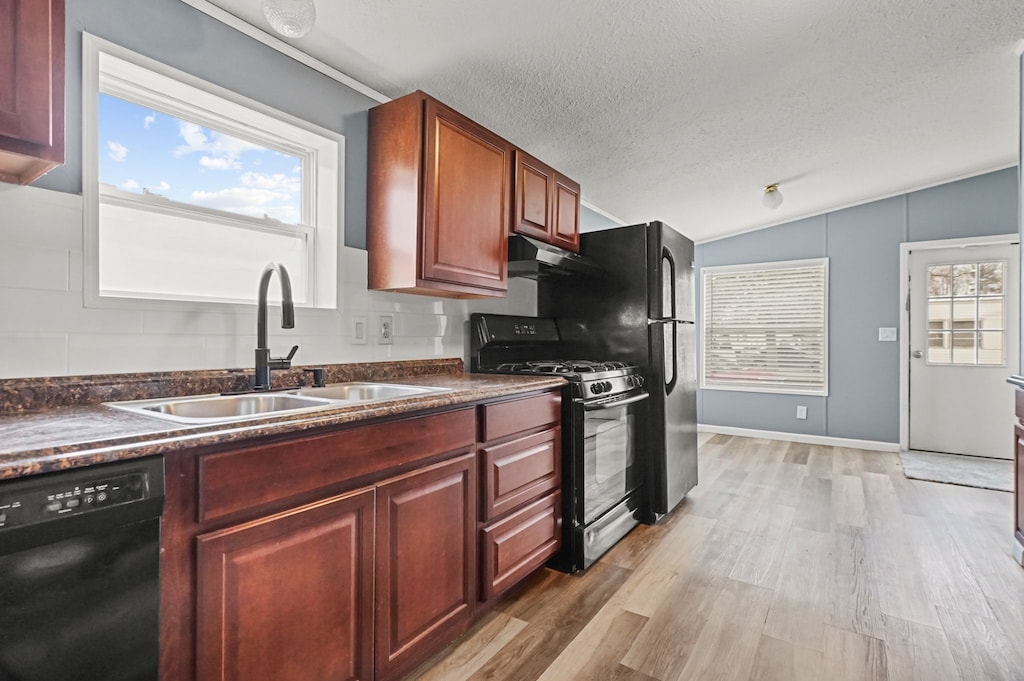 kitchen with a sink, light wood-type flooring, under cabinet range hood, dark countertops, and black appliances