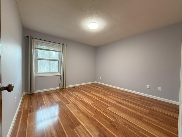 spare room with a textured ceiling, baseboards, and wood finished floors