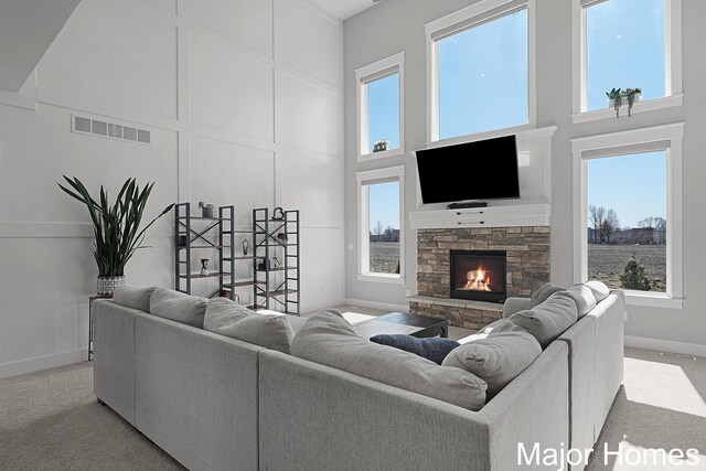 living area featuring a decorative wall, visible vents, a stone fireplace, a high ceiling, and light colored carpet
