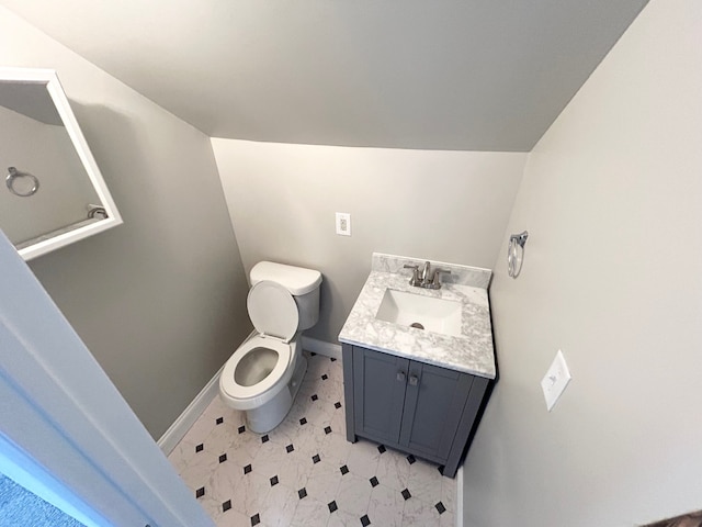 half bathroom featuring toilet, vanity, baseboards, and vaulted ceiling