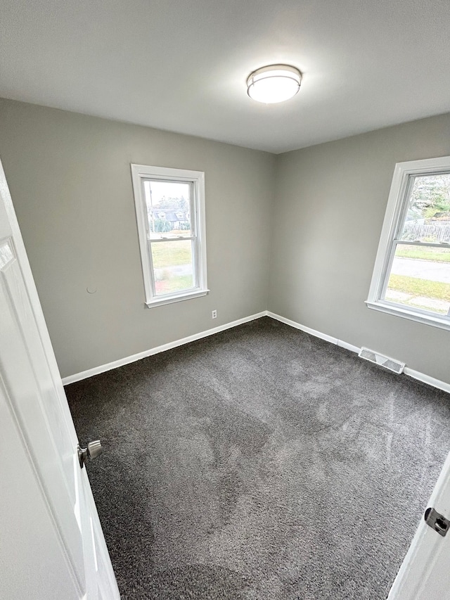 empty room with dark carpet, baseboards, visible vents, and a healthy amount of sunlight