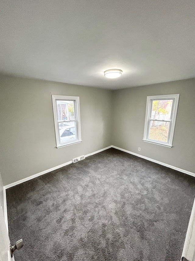 spare room with baseboards, visible vents, and dark colored carpet