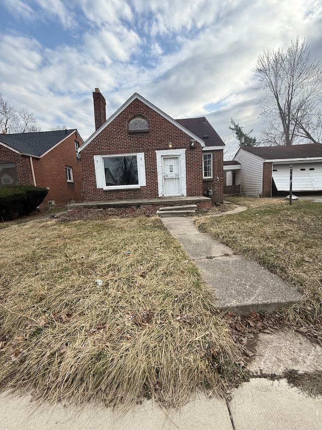 bungalow-style home featuring brick siding, a chimney, and a front lawn