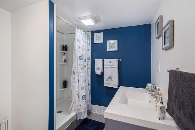 bathroom featuring baseboards, a shower stall, a sink, visible vents, and wood finished floors