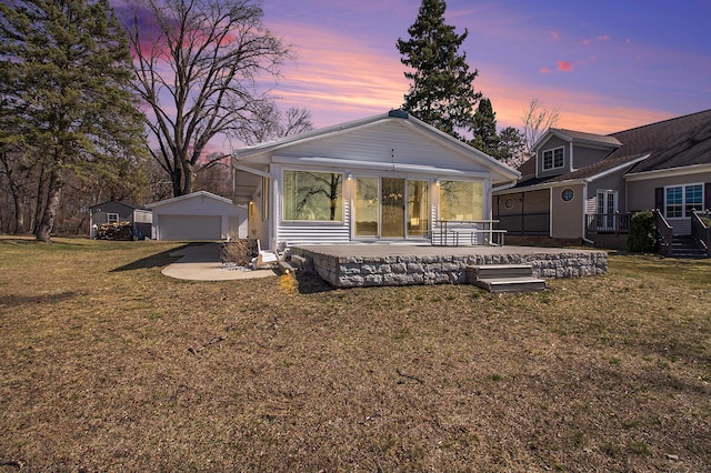 rear view of house with a lawn, a detached garage, an outdoor structure, and a patio