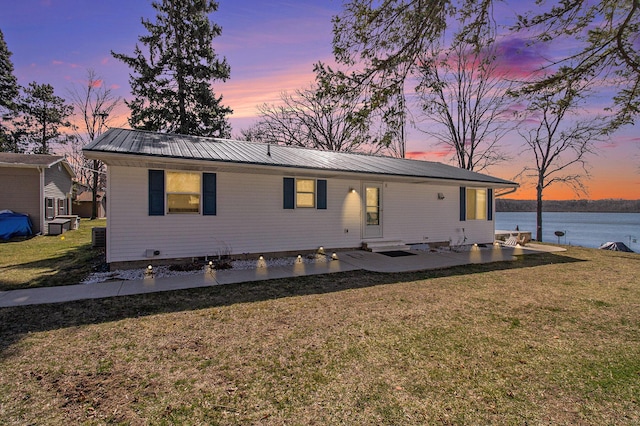 rear view of house featuring a patio, a lawn, a water view, and metal roof