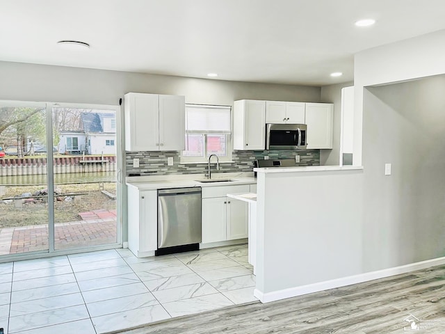kitchen featuring white cabinetry, light countertops, stainless steel appliances, decorative backsplash, and a sink