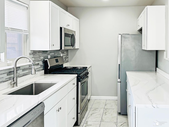 kitchen with marble finish floor, stainless steel appliances, tasteful backsplash, a sink, and light stone counters