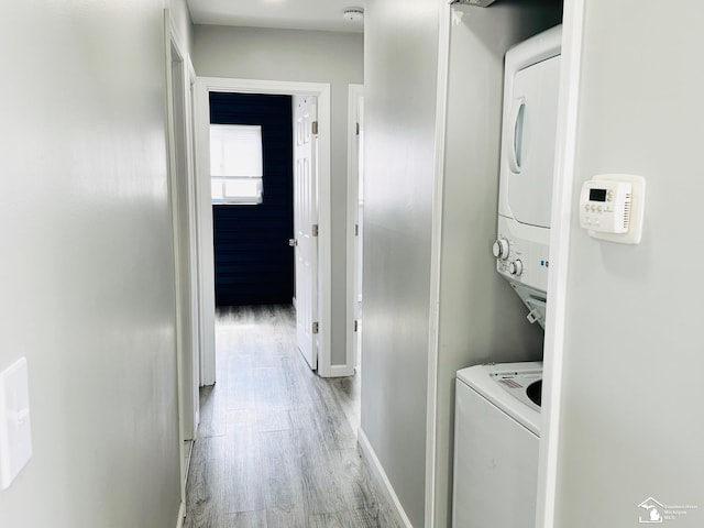 washroom featuring stacked washer / dryer, baseboards, light wood-style floors, and laundry area
