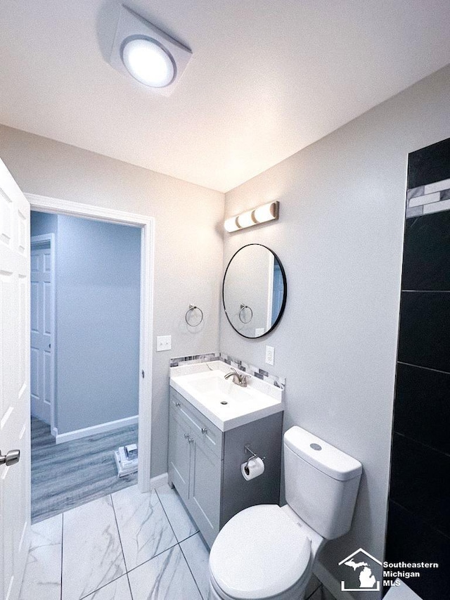 bathroom featuring marble finish floor, baseboards, toilet, and vanity